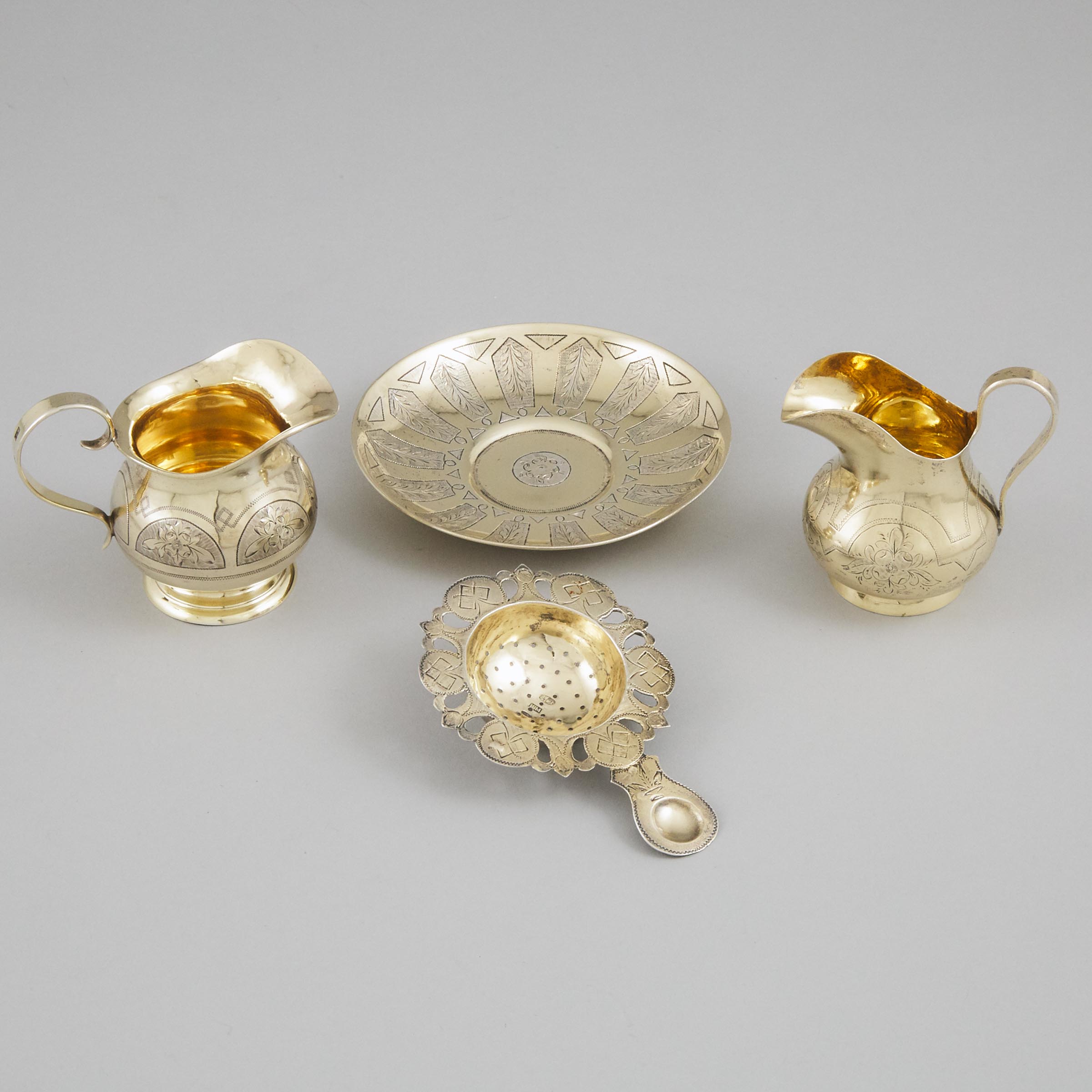 Two Russian Silver-Gilt Cream Jugs, Saucer and a Tea Strainer, late 19th century