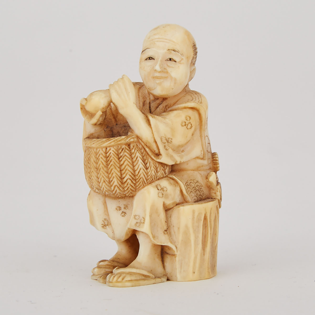 Japanese Carved Ivory Okimono Figure of a Merchant with a Basket and Bottle, early 20th century